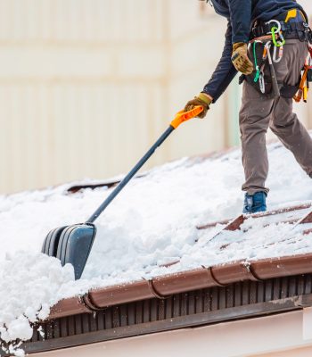 Communal services worker industrial climber removes snow from the building roof in winter. Cleaning city streets, roads and buillding roofs after snow storm in Moscow, Russia